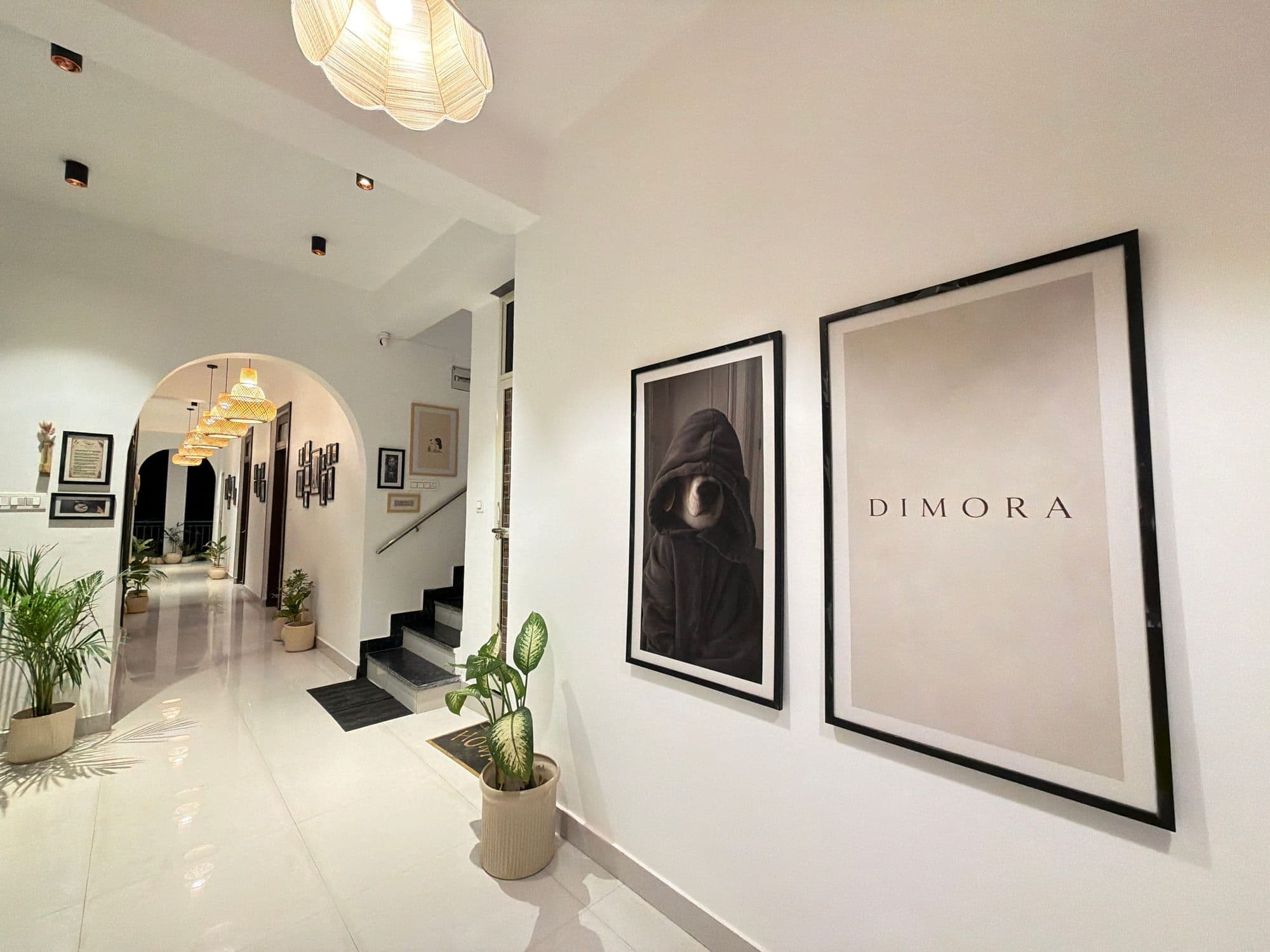 White hallway with two large framed prints, one reading Dimora, beside an arched doorway