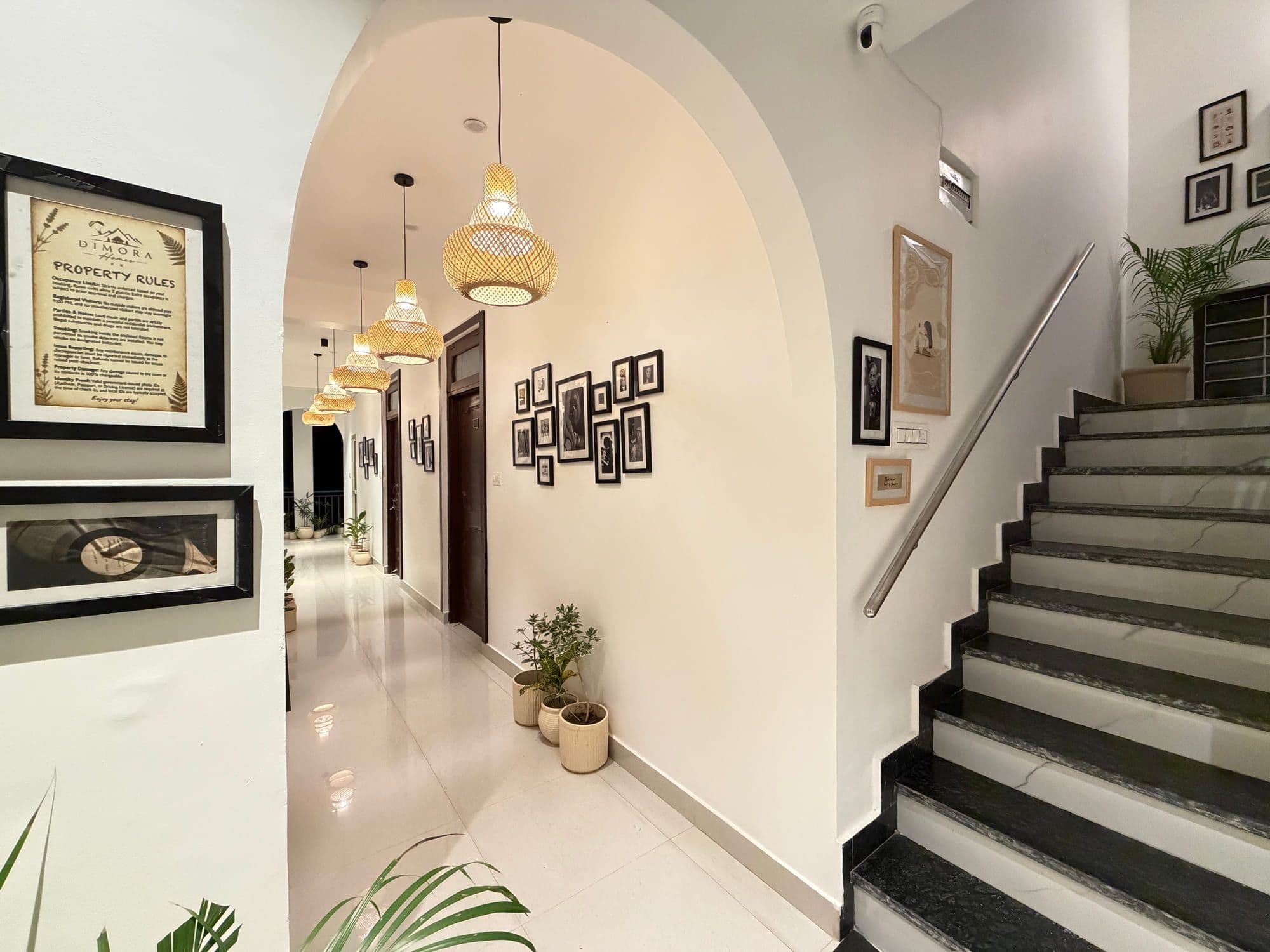 Arched passage and staircase at Dimora Homes, hung with framed pictures and lit by rattan lamps