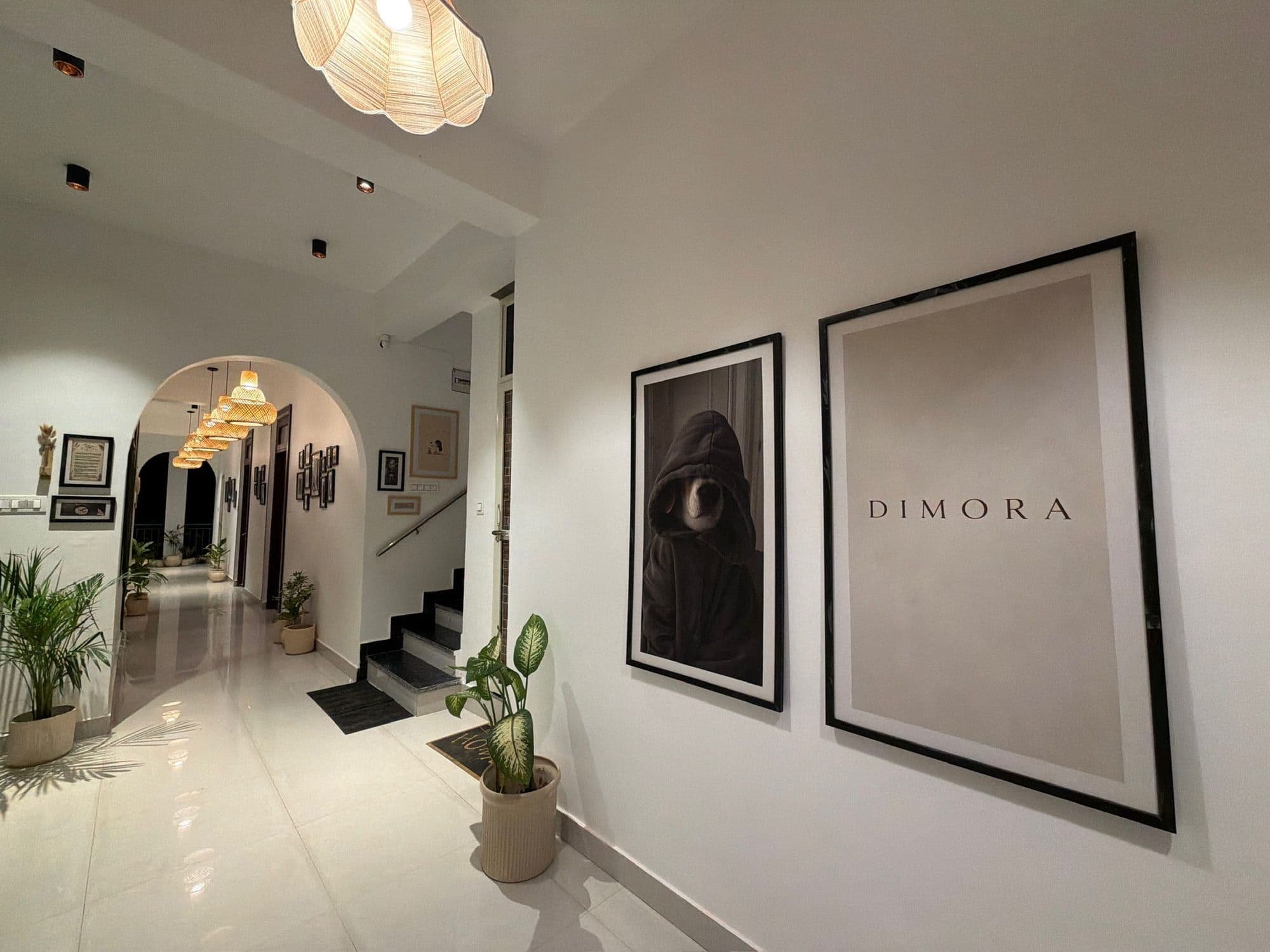White hallway with two large framed prints, one reading Dimora, beside an arched doorway