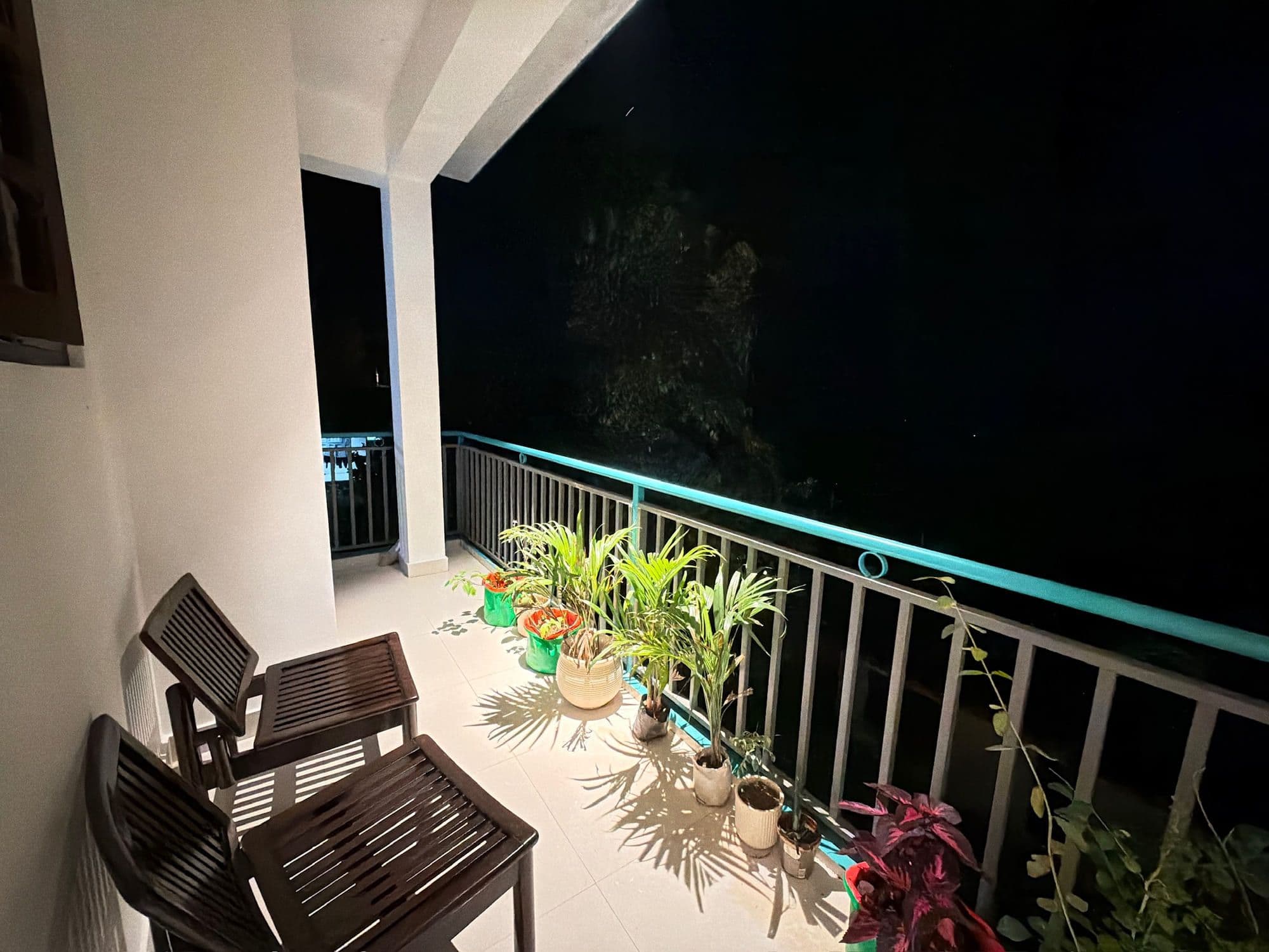 Terrace at Dimora Homes at night, with wooden seating, potted plants and a teal railing
